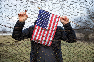 Concept of United States of America closed borders. Sad man at barbed fence., holding USA flag