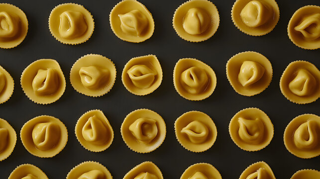 A beautiful photo of tortellini, carefully arranged in a symmetrical layout of circles, highlighting their golden color and rich texture on a dark background.