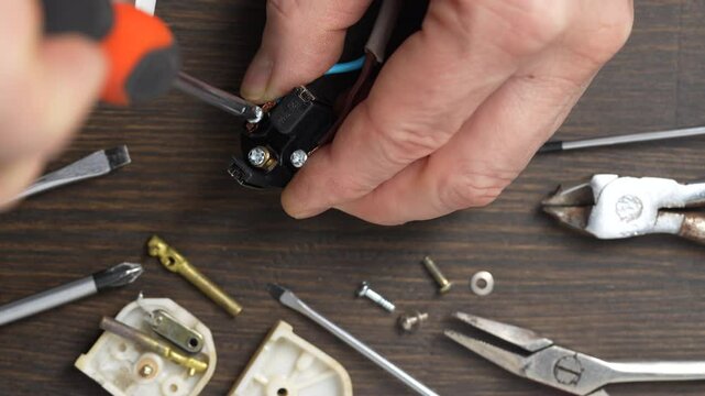 Using a Phillips screwdriver, loosen the screw on the white electrical power plug, close up. The process of parsing the body of plastic electrical plug. Repair and maintenance of electrical equipment