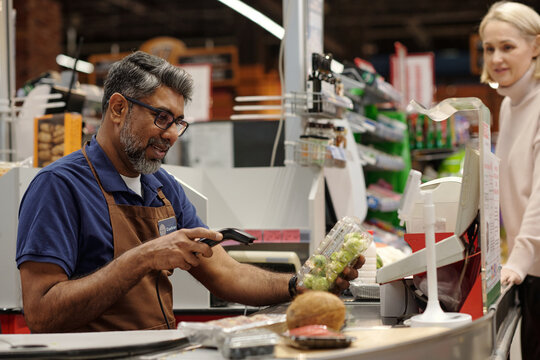 Side view portrait of smiling man scanning items while working at supermarket checkout station, copy space