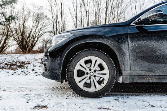 Very dirty salty black car is parked on nature covered by snow in winter.