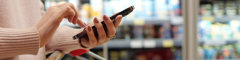 Header image of woman shopping in supermarket and using smartphone, copy space
