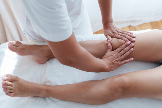 Osteopath massaging knee joints of patient in treatment room