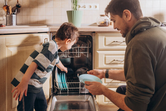 Father and son loading the dishwasher together in the kitchen