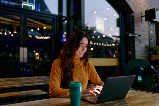 Freelancer working on a laptop at an outdoor cafe in the evening - Powered by Adobe