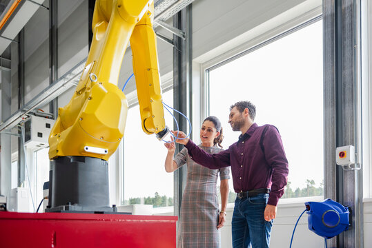 Man and woman discussing in a production hall with an industrial robot
