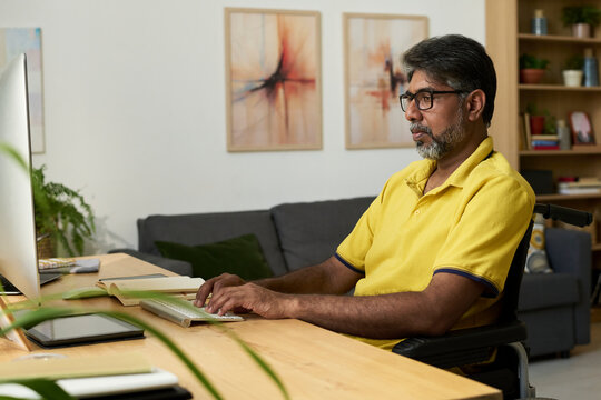 Serious man in wheelchair working at home desk in front of monitor