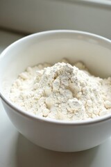 A pristine white bowl brimming with a generous mound of unbleached wheat flour, ready for baking delicious treats in a home kitchen setting.