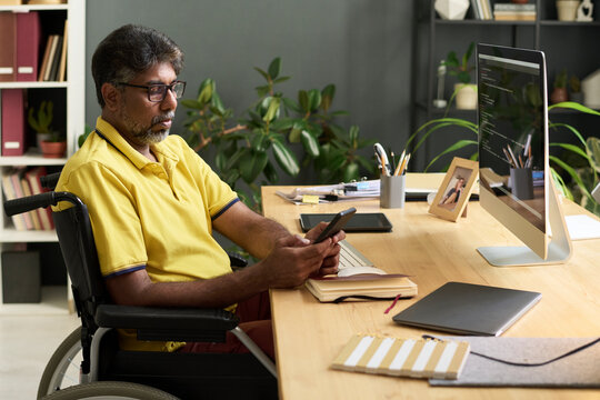 Developer in wheelchair using smartphone at office desk with colleague