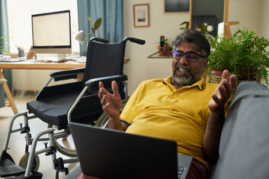 Cheerful remote worker with disability talking with colleagues on video call at home