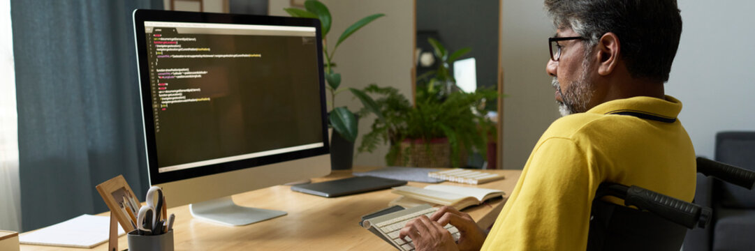 Man in a wheelchair coding at a home office desk with a computer