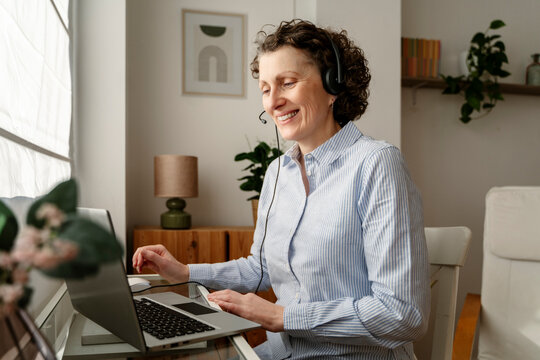 Woman working remotely in her apartment using a laptop and headset