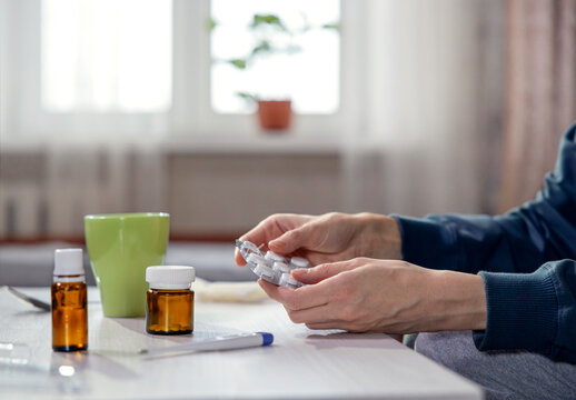 Woman holding pills with hot tea and thermometer at home