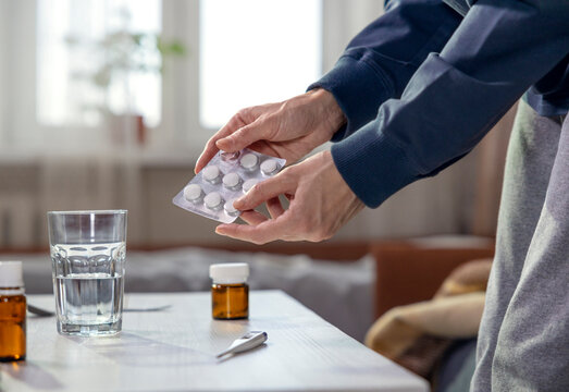 Woman's hands holding pills at home with hot tea and thermometer