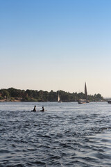 Naklejka premium Felucca sailing on Nile River and Nubian boys on surfboard in a sunny afternoon at Aswan, Egypt