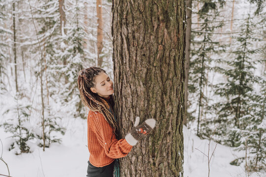 Woman with dreadlocks hugging a tree in a snowy forest, expressing unity with nature