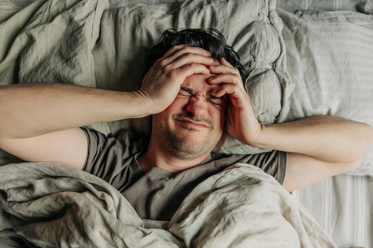 Man with headache lying in bed in the morning with hands on head