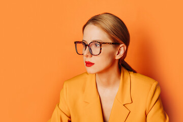 Stylish businesswoman in yellow jacket with glasses against orange background