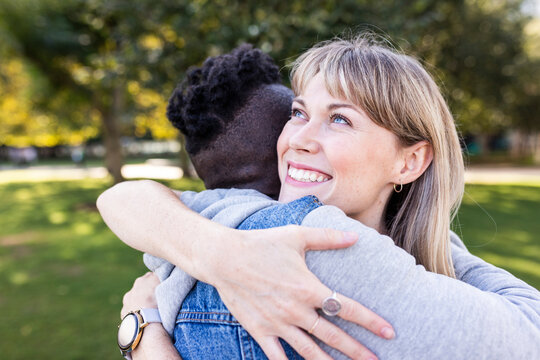 Thoughtful smiling woman embracing friend at park