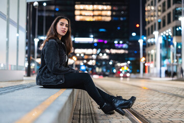 Woman sitting on a city sidewalk at night waiting