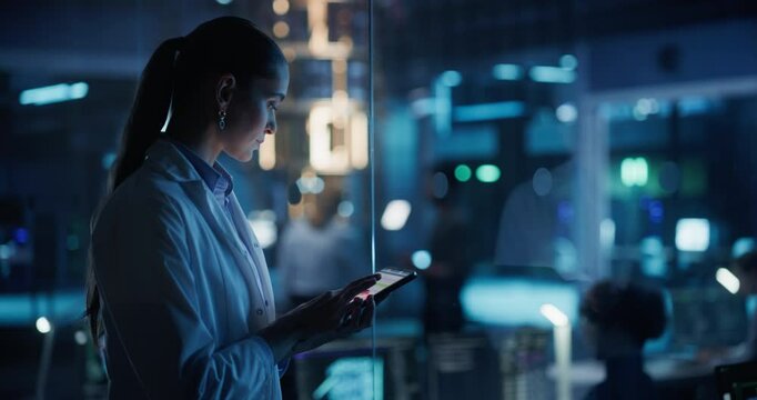 Female Scientist Using a Tablet to Monitor the Work of a Quantum Computer, Focusing on Data Flow, Compute and Hardware Stability. Futuristic Dark Setting with Advanced Technological Office
