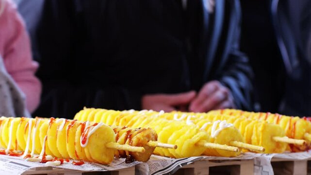 Twist, tornado, or spiral potato - traditional Asian street food snack, skewer, close-up. Crispy potato cut spiral and deep-fried, served with sauces ketchup or mayo at market