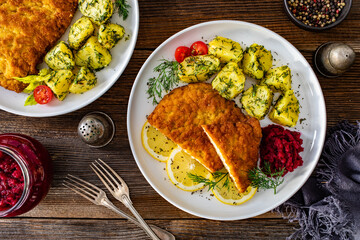 Breaded fried pork chop with boiled potatoes and beets on wooden table	