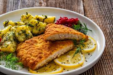 Breaded fried pork chop with boiled potatoes and beets on wooden table	