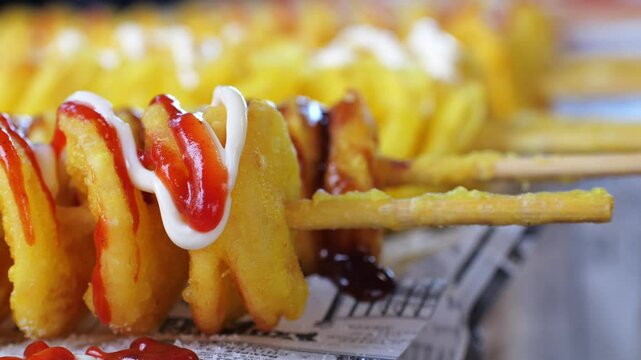 Twist, tornado, or spiral potato - traditional Asian street food snack, skewer, close-up. Crispy potato cut spiral and deep-fried, served with sauces ketchup or mayo at market