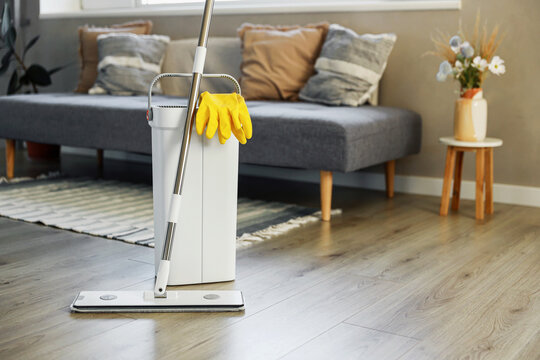 Cleaning supplies: mop, gloves, bucket with wringer sitting on wooden laminate floor in modern living room, wet equipment tools, housekeeping concept. Emphasizing home sanitation, cleanliness, hygiene