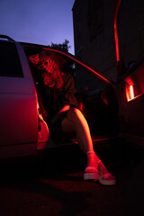 Chic figure confidently poses in a car, surrounded by a vibrant urban night scene