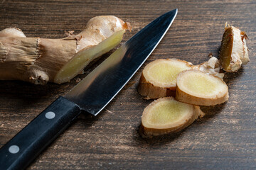 Cutting ginger root into pieces with a knife on a wooden cutting board, closeup