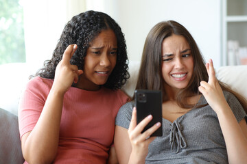 Worried friends crossing fingers checking phone