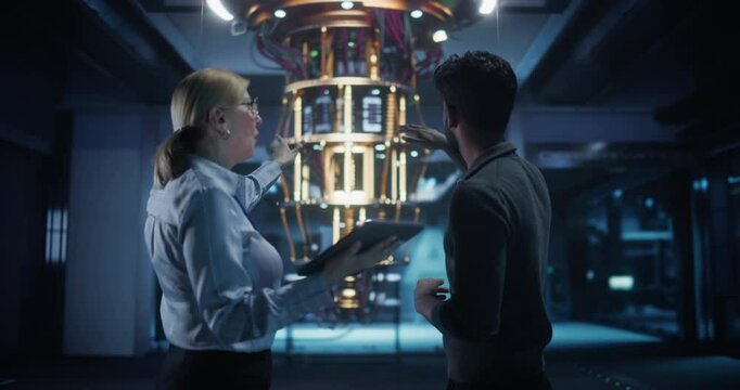 Middle Aged Caucasian Female Team Leader and Young Indian Scientist Talking in a Research Center with a Futuristic Quantum Computer Device. Specialists Discussing Machine Learning Development