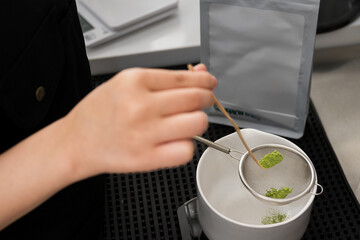 Barista making green tea in to white cup at the coffee shop.Close up hand while preparing matcha menu from green tea powder on black background.