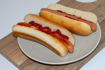 Juicy hot dogs nestled in soft buns are displayed on a round plate. One hot dog is topped with ketchup while the other is enhanced with mustard, perfect for a casual meal