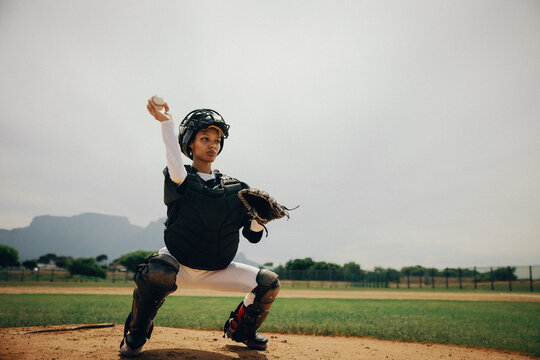 Female baseball catcher crouching in outfield ready to throw ball during sunny day practice - Powered by Adobe