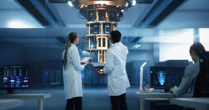 Young Caucasian Female Team Leader and Male Indian Scientist Talking in a Research Center with a Futuristic Quantum Computer Device. Specialists in White Coats Standing with Their Backs to Camera