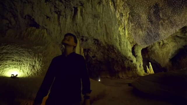 Man Explorer in an Illuminated Underground Cave with Stalactites