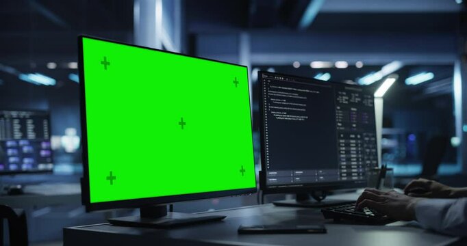 Anonymous Software Developer Working Behind a Desk on a Computer with Green Screen Chromakey Display. Engineer Writing Source Code, Creating Software for a Technological Online Product