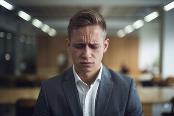 Fototapeta premium Stressed businessman in suit looking down in modern office environment