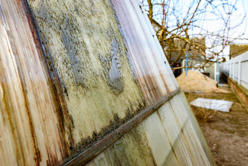 Close-up of a greenhouse wall made of old worn out dirty polycarbonate full of holes.