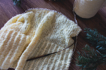Yellow knitting pattern with coniferous tree branch on wooden table. Knitted fashion. Cotton knitting crochet with knitting needles. Knitting hobby. Handmade knitted clothing. Cozy winter still life.