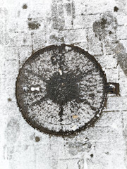  snow-dusted manhole cover, a dark circle on a textured, white surface. Capture the contrast of urban infrastructure against the delicate touch of winter's first snow.