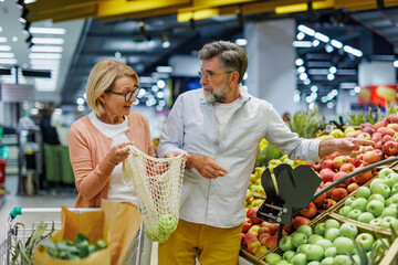 Senior couple choosing apples using reusable shopping bag at grocery store