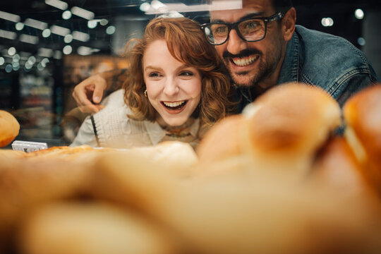 Happy couple choosing bread in supermarket bakery display,