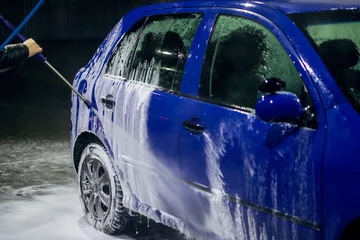 A man wearing a black jacket is cleaning and washing a blue car