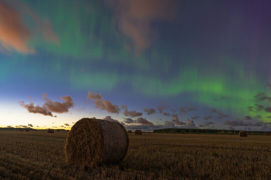 Mesmerizing aurora borealis over a field with a sheaf of hay. The starry sky and mystical green glow create a magical atmosphere in the night landscape.