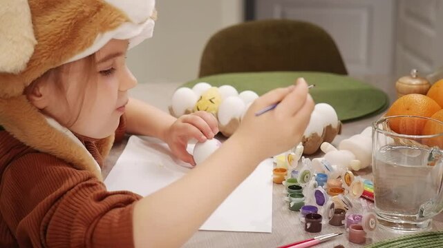 Young girl wearing fox costume painting easter eggs at home
