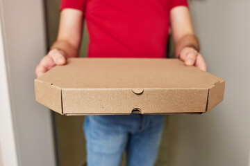 hands of delivery man in red t-shirt giving food order and holding pizza box at home